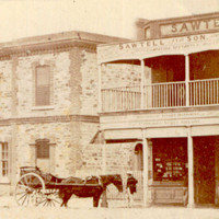 Image: A horse-drawn cart parked in front of three bluestone buildings. 