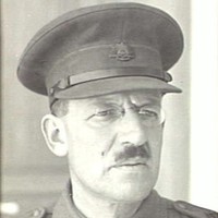 Image: A moustachioed middle-aged Caucasian man in an Australian Army officer's uniform. He is wearing a hat and spectacles with oval lenses