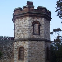 Image: A two-storey octagonal stone tower set within a high wall with a crenellated parapet.