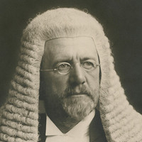 Image: A photographic head-and-shoulders portrait of a bearded middle-aged Caucasian man wearing a judicial wig and vestments. He is also wearing wire-rimmed spectacles and looking to his left