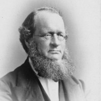 Image: Black and white photographic portrait of a man with small round glasses and a large beard