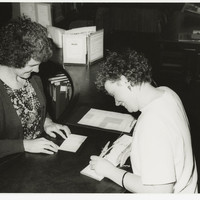 Image: two smiling caucasian women writing at a main desk in library
