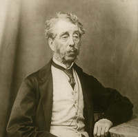 Image: Black and white portrait of a man with grey hair, mutton chops and a moustache. He is wearing a suit jacket, vest, shirt and tie.