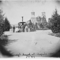 Image: Two young girls and a row of young men are leaning against a fountain in front of a church