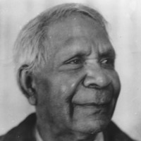 Image: A photographic head-and-shoulders portrait of an elderly Aboriginal man. He is clean-shaven, sporting a short haircut and is wearing a suit jacket and tie