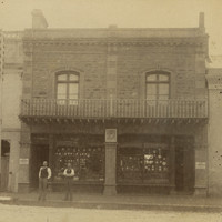 Image: Two men in Victorian attire stand in front of a two-storey brick and bluestone building