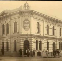 Image: sepia shot of building facade, with three men at the entrance, one by the side, and a horse-drawn carriage