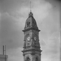 Image: A tall stone clock tower with an ornate roof and flagpole at its peak