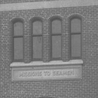 Image: A large, two-storey brick building built in mock-Tudor style, with two turrets flanking a large entrance door. A sign reading ‘Missions to Seamen’ is visible above the entrance door