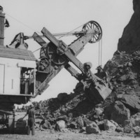 Image: two men operating large machinery inf fron of pile of boulders
