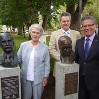 Image: Three people standing with two bronze busts