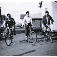 Image: three men riding bicycles between buildings