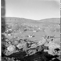 Image: man sitting on rocky outcrop overlooking township