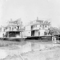 Image: Black and white photograph of two paddlesteamers anchored next to each other on a river. The paddlesteamer on the left is flying the Union Jack