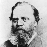 Image: A photographic head-and-shoulders portrait of a middle-aged Caucasian man with a bushy salt-and-pepper beard and receding ear-length hair. He is wearing a late-Victorian suit with bowtie