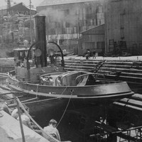 Image: A tugboat sits on stands in a dry-dock. A group of men sit facing the vessel in the foreground