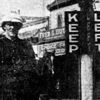Image: A Caucasian man in an early twentieth century police uniform stands next to a marker with the words ‘Keep’ and ‘Left’ painted on it in large block letters