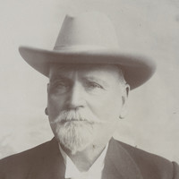 Image: A photographic portrait of an elderly Caucasian man with a white goatee. He is wearing a Stetson hat and a dark-coloured overcoat