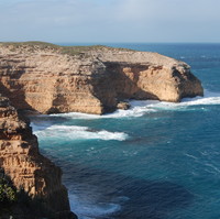 Image: A large bare cliff face juts out into the ocean