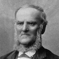 Image: A photographic portrait of a middle-aged balding man in Victorian attire. He is sporting a long chin-beard