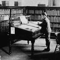 Image: A small group of men in a book-filled library read from desks