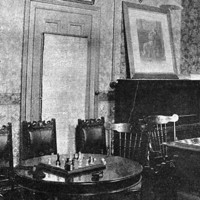 Image: Three chess tables with chairs stand in a room decorated with wallpaper and framed portraits