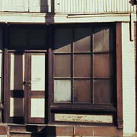 Image: A two-storey building with brick first floor and corrugated metal second floor stands derelict next to a city street