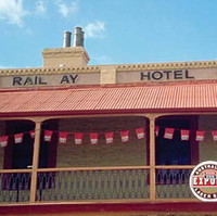 Image: Colour photograph of a two-storey late Victorian-era building on the corner of two paved streets. The building is painted tan with red trim and has the words ‘Rail ay Hotel, 1856’ painted beneath its roof