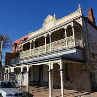 Image: two story brick building with painted ironwork and veranda