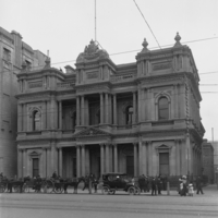 Image: horse carts and car in front of ornate bank building