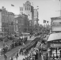 Image: Military parade down a main street, with tall buildings in the background