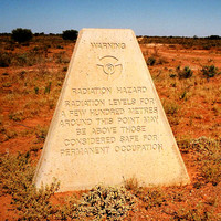 Image: A pyramidal-shaped concrete plinth stands in a vast, open desert area. A notation inscribed on the plinth warns of radioactive contamination