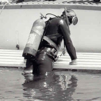 Image: A scuba diver exits the water at the stern of a small motor boat. Two police officers aboard the boat look on