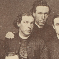 Image: A group of Caucasian men in mid-Victorian Catholic clergymen outfits pose for a photograph in a studio. The younger men in the group stand behind four older men who are seated