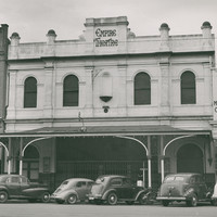 Image: 1950s era cars are parked on the street outside a two-storey terraced building with arched windows, a balcony and a stepped parapet with a sign reading Empire Theatre