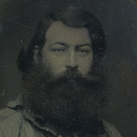 Image: a head and shoulders portrait of a man with long dark hair and a very thick long black beard. He is wearing a casual 1850s era shirt.
