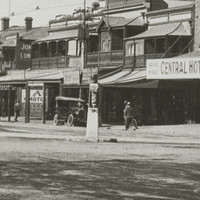 Image: An intersection of two streets in an urban area. A plinth with the words ‘Keep Left’ stands in the centre of the intersection. Early twentieth century cars and a horse and cart are parked in the background