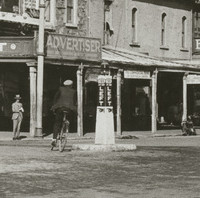 Image: A man in early twentieth century attire rides a bicycle around a plinth in the centre of an intersection. The words ‘Keep to the Left’ are painted on the sides of the plinth. Several early twentieth century cars are visible in the background 