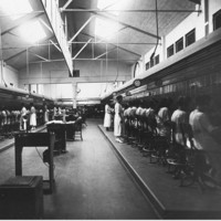 Image: A telephone exchange. There are two rows of switchboard operators on either side of the image, separated by a floor and desks.