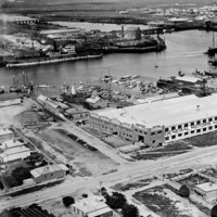 Image: An aerial photograph of a port town, at the centre of which is a large building with the words ‘General Motors Aust. Pty. Ltd’ emblazoned across it. Sailing and motor vessels of various types are visible in the river beyond the building