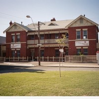 Image: A two-storey brick building with signs advertising the Salvation Army stands near the edge of a park