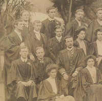 Image: A large group of Caucasian men and women in early Edwardian attire pose for a photograph in front of a stand of trees. All are wearing academic graduate gowns. A notation at the top of the photo reads: ‘University Training College, 1905’ 