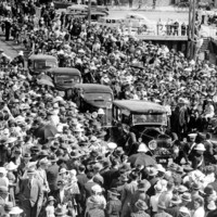 Image: Four 1940s-era auto-mobiles move through a crowd of people gathered for a ceremony