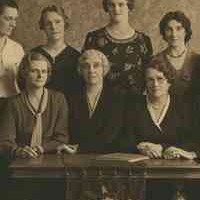 Image: A group of women are gathered around a table. The front row is seated, while those in the back row stand