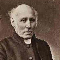 Image: Photograph of bald seated man wearing a dark coloured coat and clerical collar 