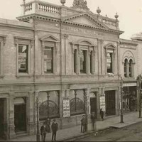 Image: a two storey theatre building, part of a longer terrace, with a decorative parapet featuring stone urns, a lion and a unicorn