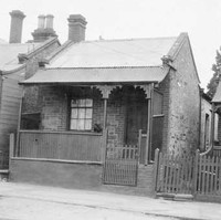 Image: a row of tiny stone workers cottages with brick quoins, a single door and window beneath a verandah on the front elevation, pitched tin roofs and small lean-tos on the rear.