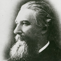 Image: The head and shoulders of a middle-aged man with long hair and a large goatee in profile. The left side of the man’s face is visible  
