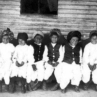 Image: A group of children in traditional Afghan clothing sit on the verandah of a rural home 
