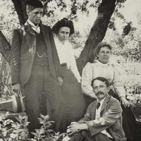 Image: A moustachioed man in a suit sits on a rug. Leaning against a tree behind him are a young man, young woman, and and adult woman in Edwardian attire